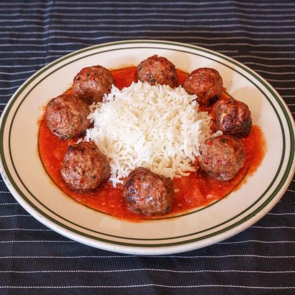 Moustache Pitza's meatballs and rice, served in a rich red sauce on a white plate with green trim.