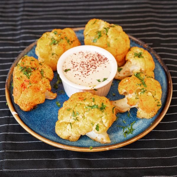 Golden fried cauliflower florets with a side of creamy dip, garnished with sumac and parsley.