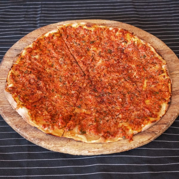 A round, sliced Moustache Pitza lahmacun with red meat topping on a wooden board.