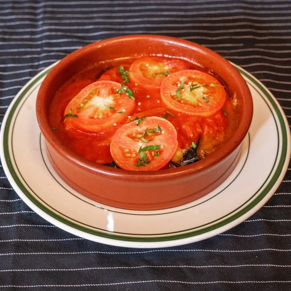 A terracotta bowl of Moustache Pitza's middle-eastern dish with tomato slices and herbs.