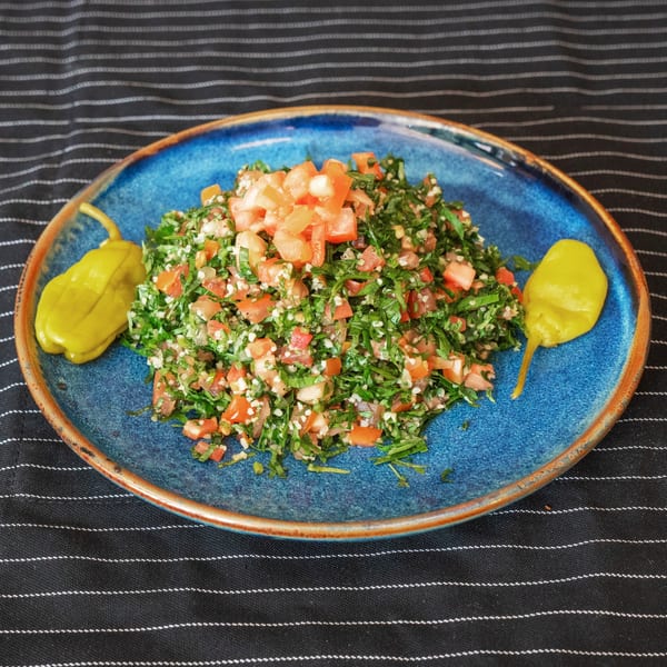 Moustache Pitza's tabbouleh salad with diced tomatoes, parsley, and two yellow peppers on a blue plate.